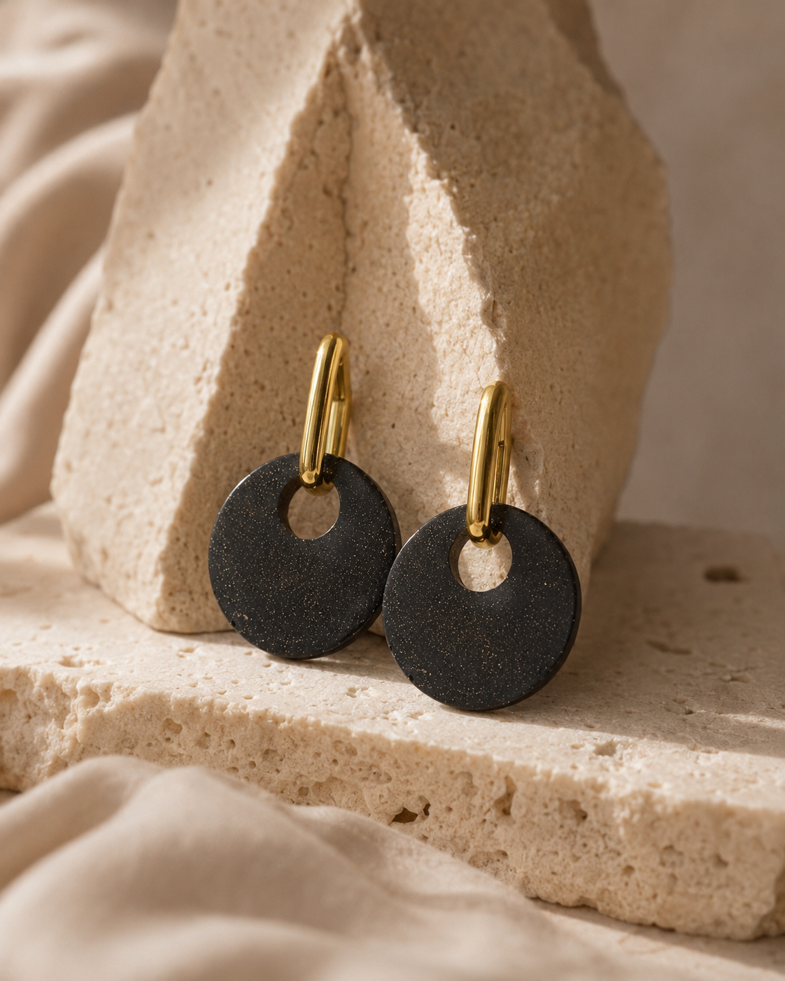 Close-up of Lou earrings, handmade from recycled coffee grounds and real gold powder, styled on a textured neutral surface with gold-plated findings.