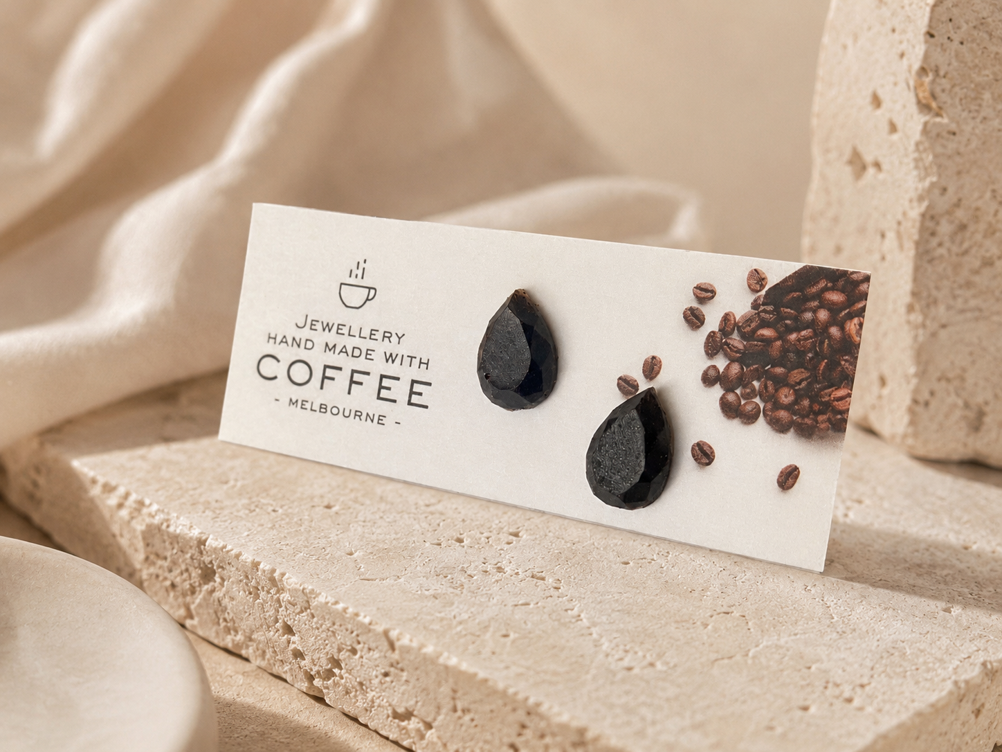 Drop recycled coffee-stone earrings displayed on an Atelier Cayelle card with coffee beans and stone texture.