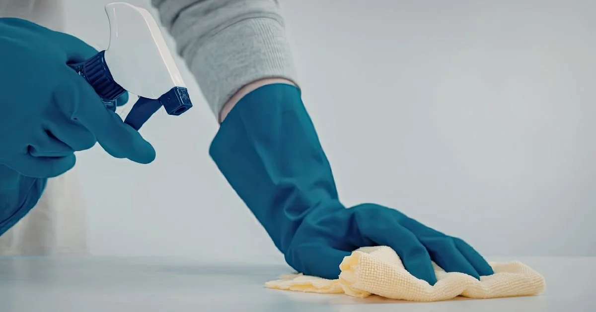 cleaner wearing blue gloves, holding a spritz bottle of cleaner and wiping down a table