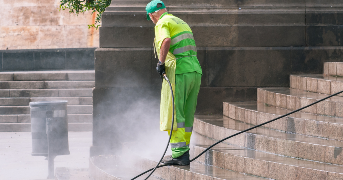 man in green coveralls power washing stairs