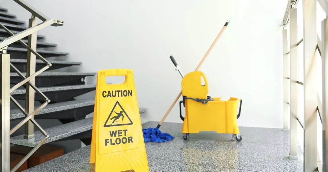 A staircase with slippery floors, a mop and janitor bucket nearby with a caution wet floor sign