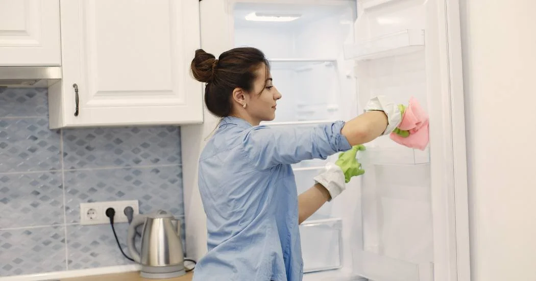 A woman cleans out a refrigerator in an office