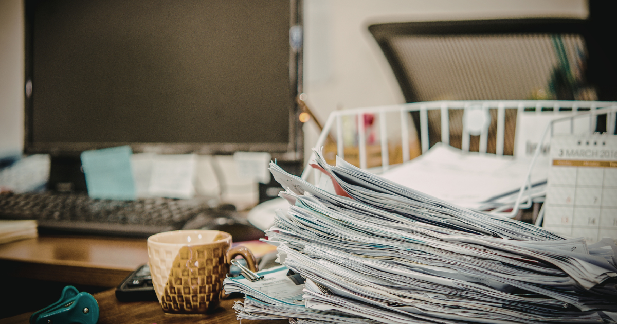 A stack of scattered papers, mugs, post-its, and other office supplies on a desk