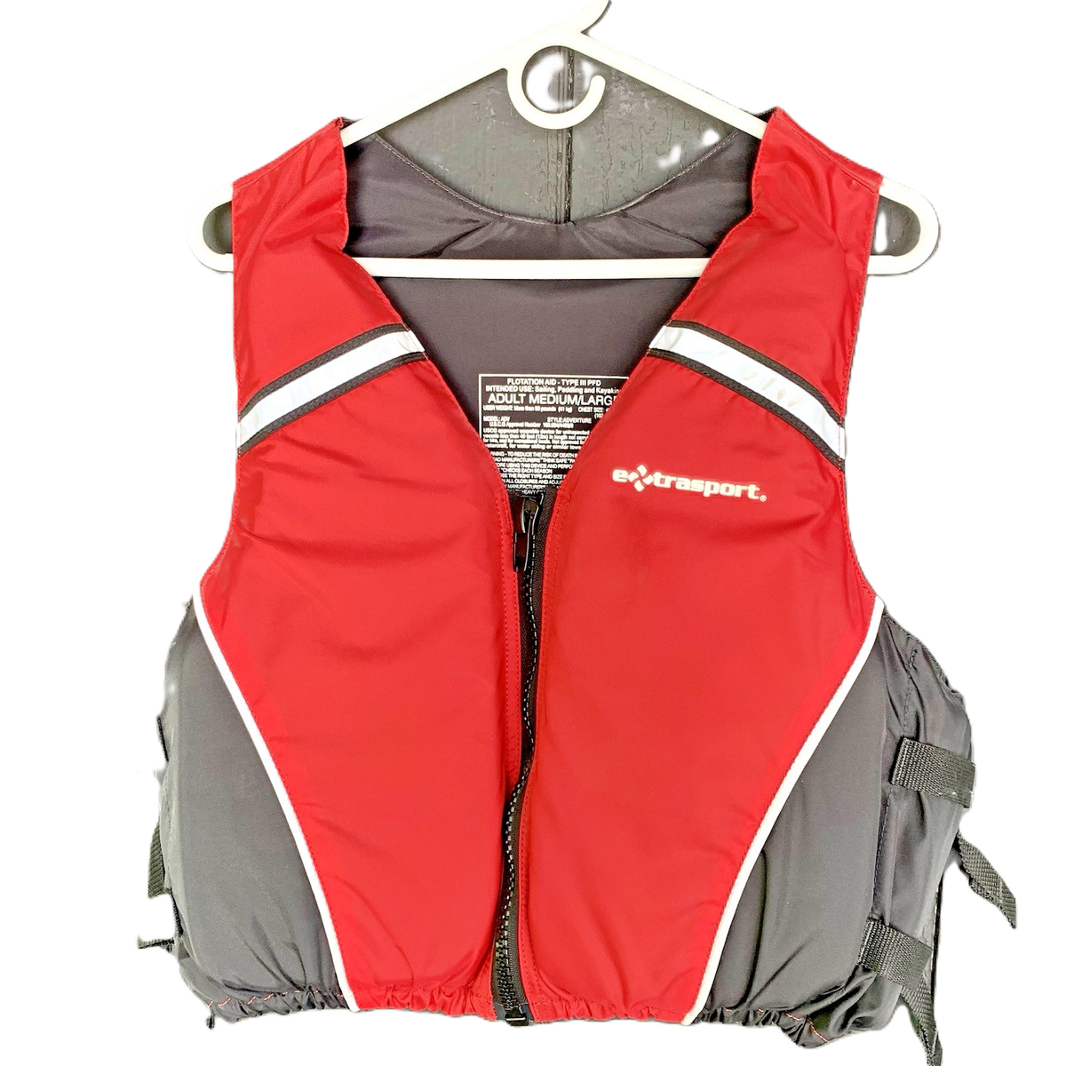 Red and gray life vest with black and white stripes hanging on a white hanger.