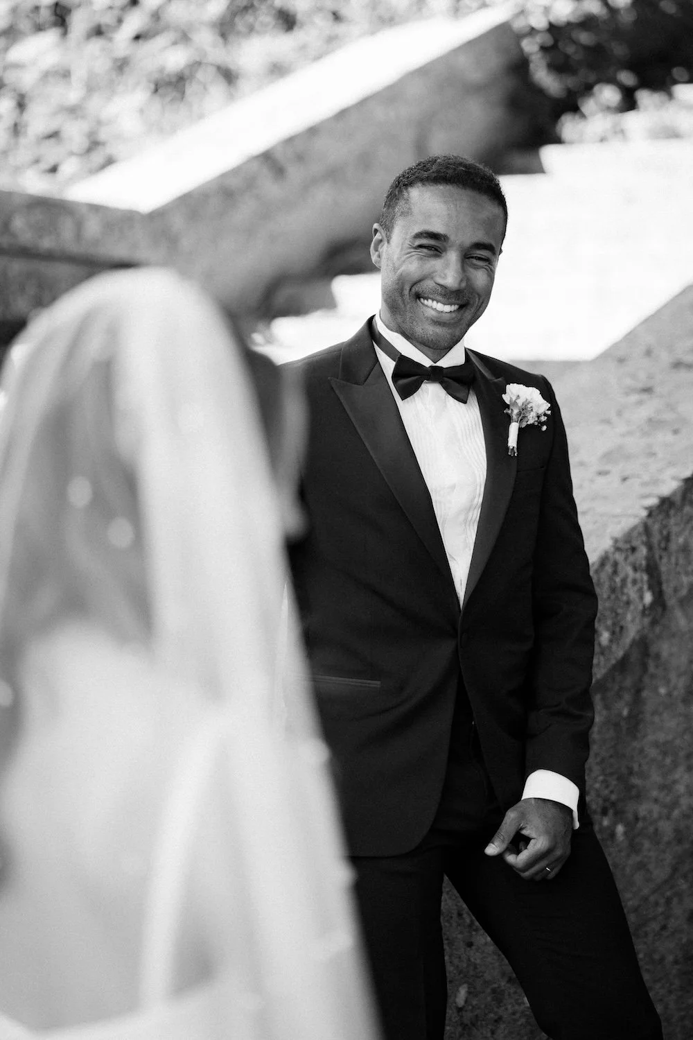 Mustasulkisessa puvussa oleva mies hymyilee ja katsoo kohti naista, jonka hiukset näkyvät etualalla.