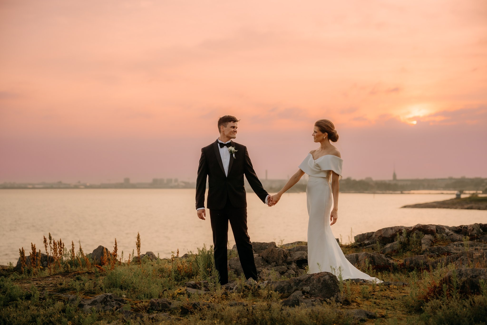 Pariskunta käsi kädessä rannalla auringonlaskun aikaan.