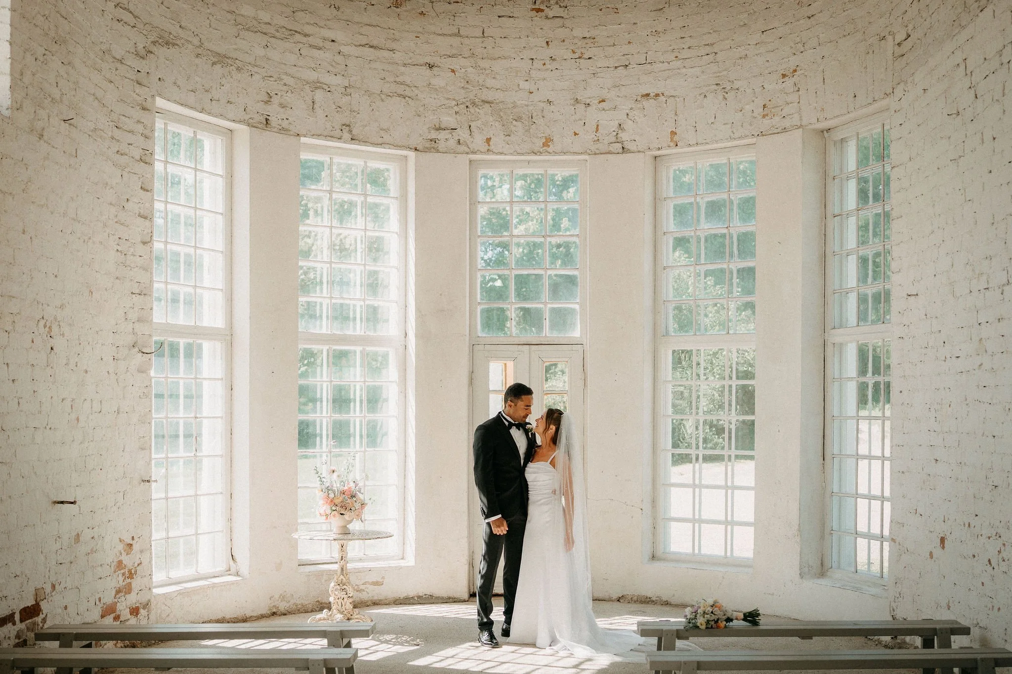 Häätanssijat seisovat vastakkain suurissa ikkunaluukuissa, valkoinen seinä taustalla.