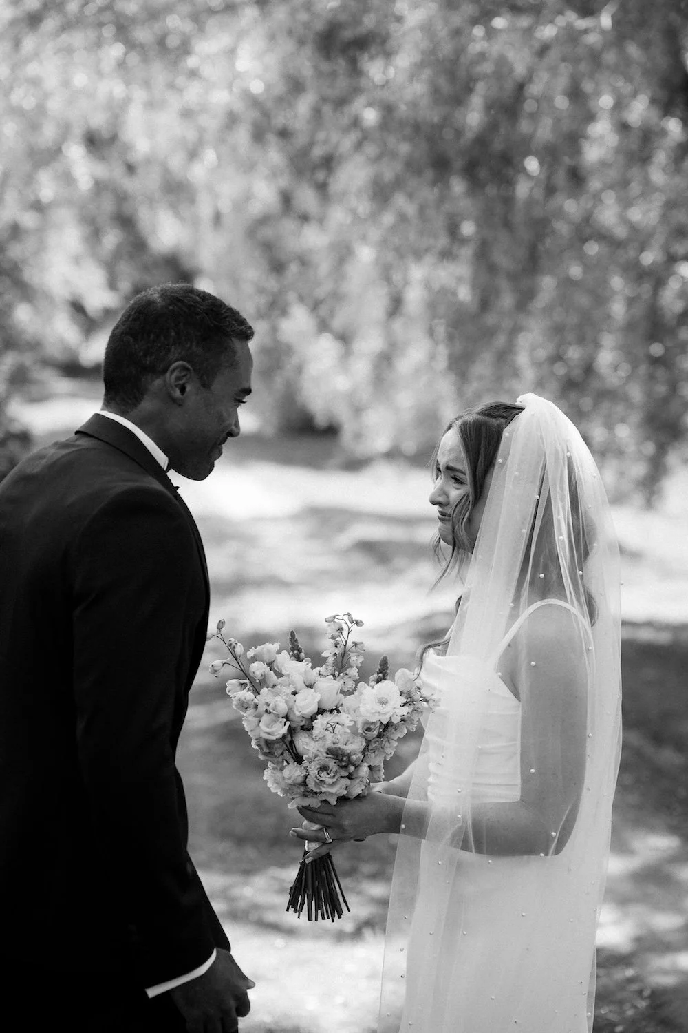 Morsian ja sulhanen katsovat toisiaan tunteellisessa hetkessä ulkona, morsian pitää kukkaseppelettä.