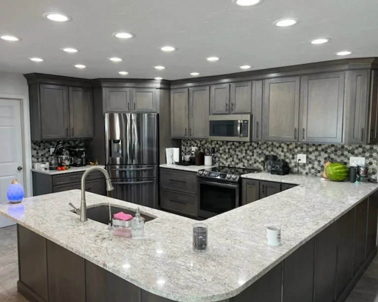 Modern kitchen with gray cabinets, granite countertops, stainless steel appliances, and a black stove. Items on the counter include a watermelon, a coffee machine, and cleaning supplies.