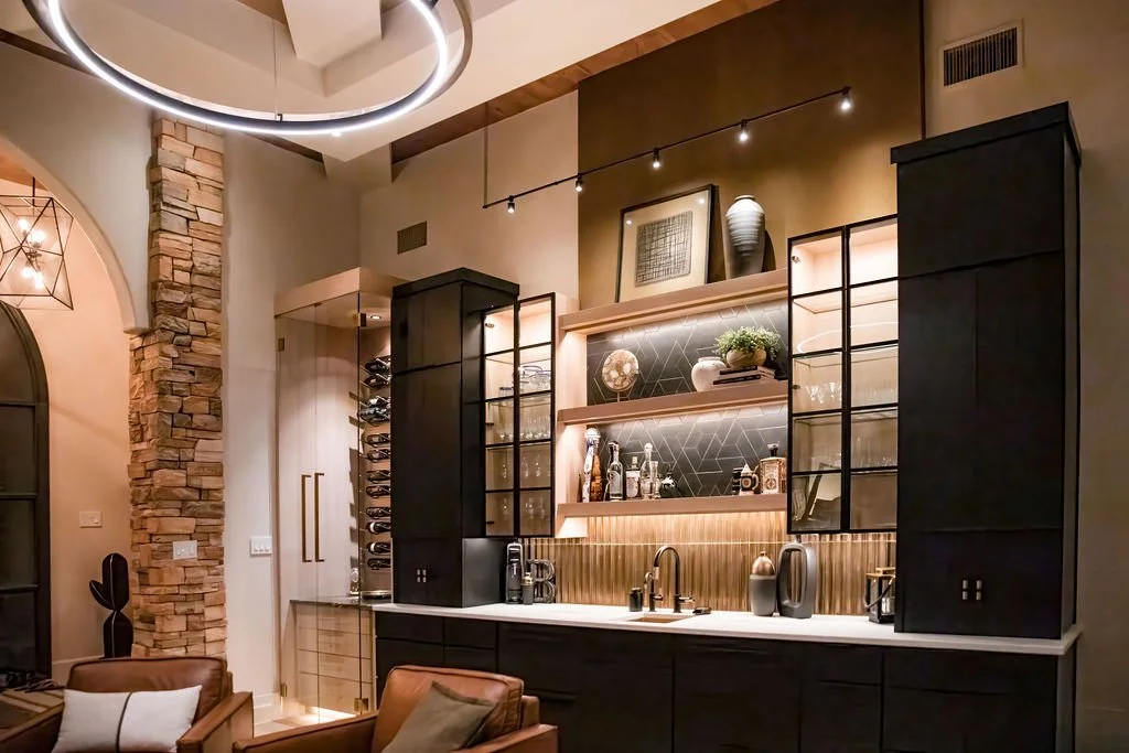 Modern kitchen with a stone wall, black cabinets with glass doors, open shelves with decorative items, and a built-in wine rack, illuminated by stylish lighting fixtures.