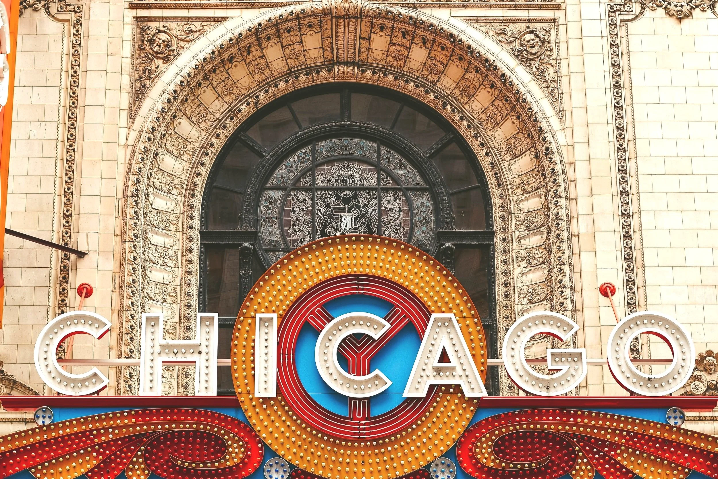A vintage Chicago theater sign with bright lights and ornate architecture in the background.