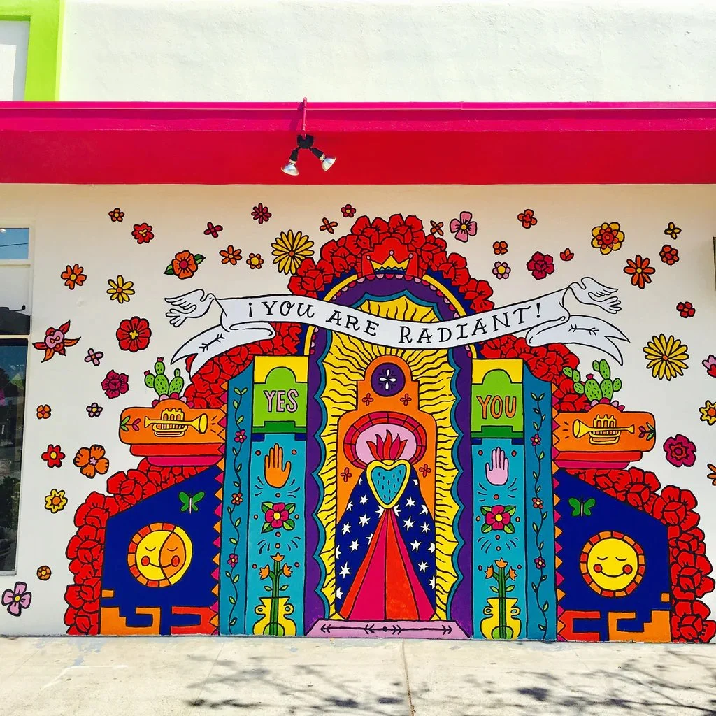 Colorful mural with a central candle, surrounded by flowers, musical instruments, and symbols of positivity. Banner at top reads 'You Are Radiant!'