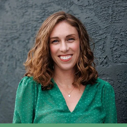 Photo of Elly Grogan wearing a green shirt in front of a dark grey wall