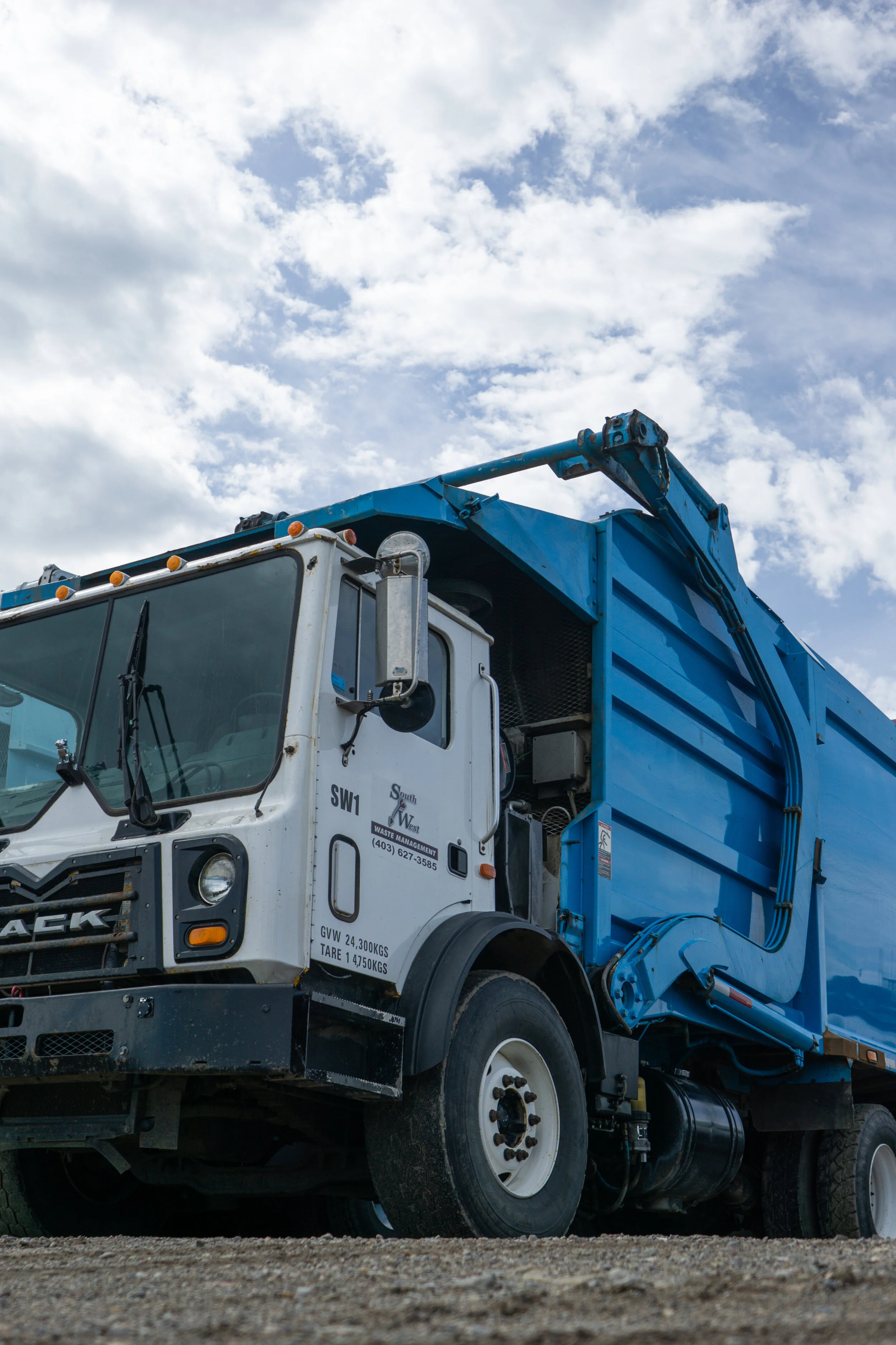 A white and blue garbage truck parked outdoors under a partly cloudy sky.