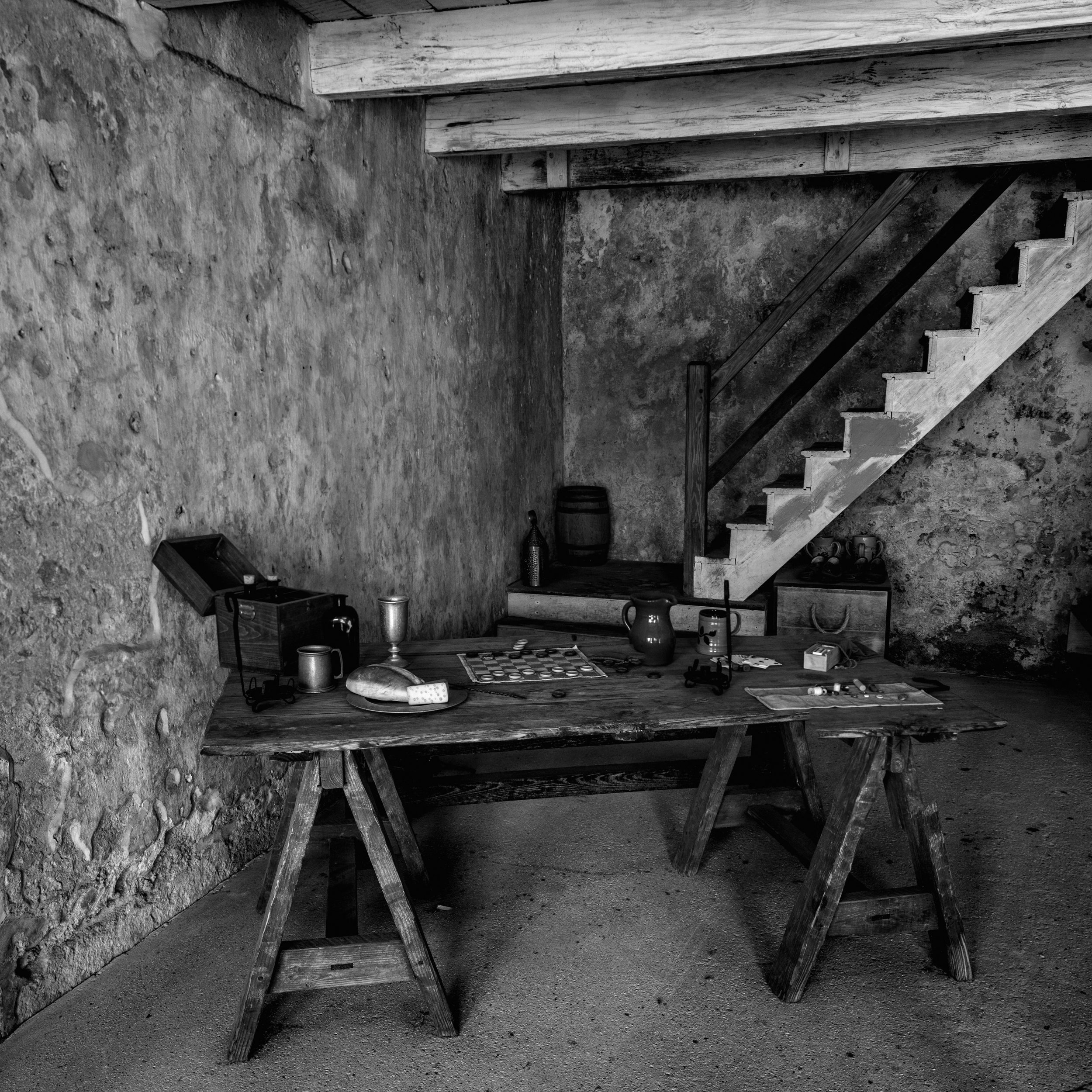 An old rustic room in Castillo de San Marcos showing a Spanish era furnishings with a wooden table and stairs, decorated with various vintage items and bottles. St Augustine Florida