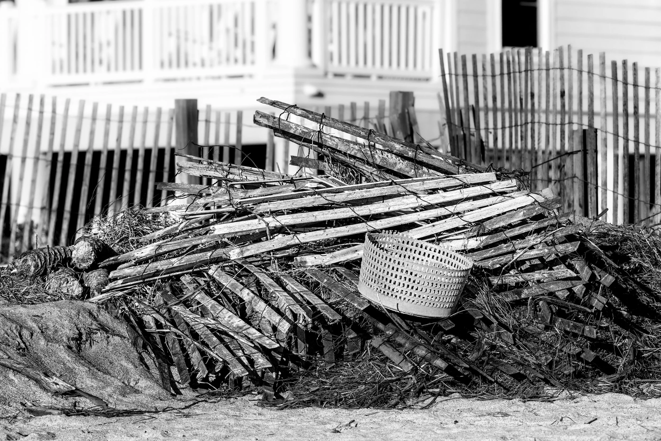 Pile of broken wooden slats, a plastic basket, and debris in front of a damaged wooden fence. Vilano Beach Florida after a hurricane