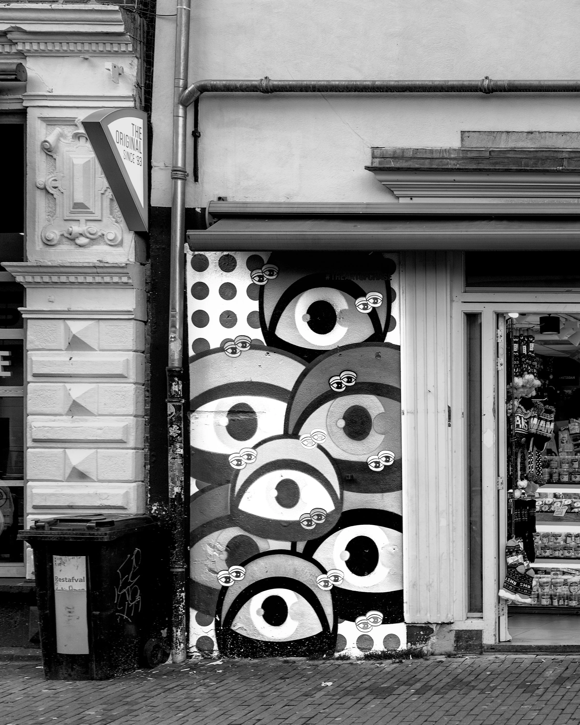 Street mural featuring multiple stylized eyes with glasses, surrounded by polka dots, on a building wall in black and white. Amsterdam, Netherlands. Hasselblad