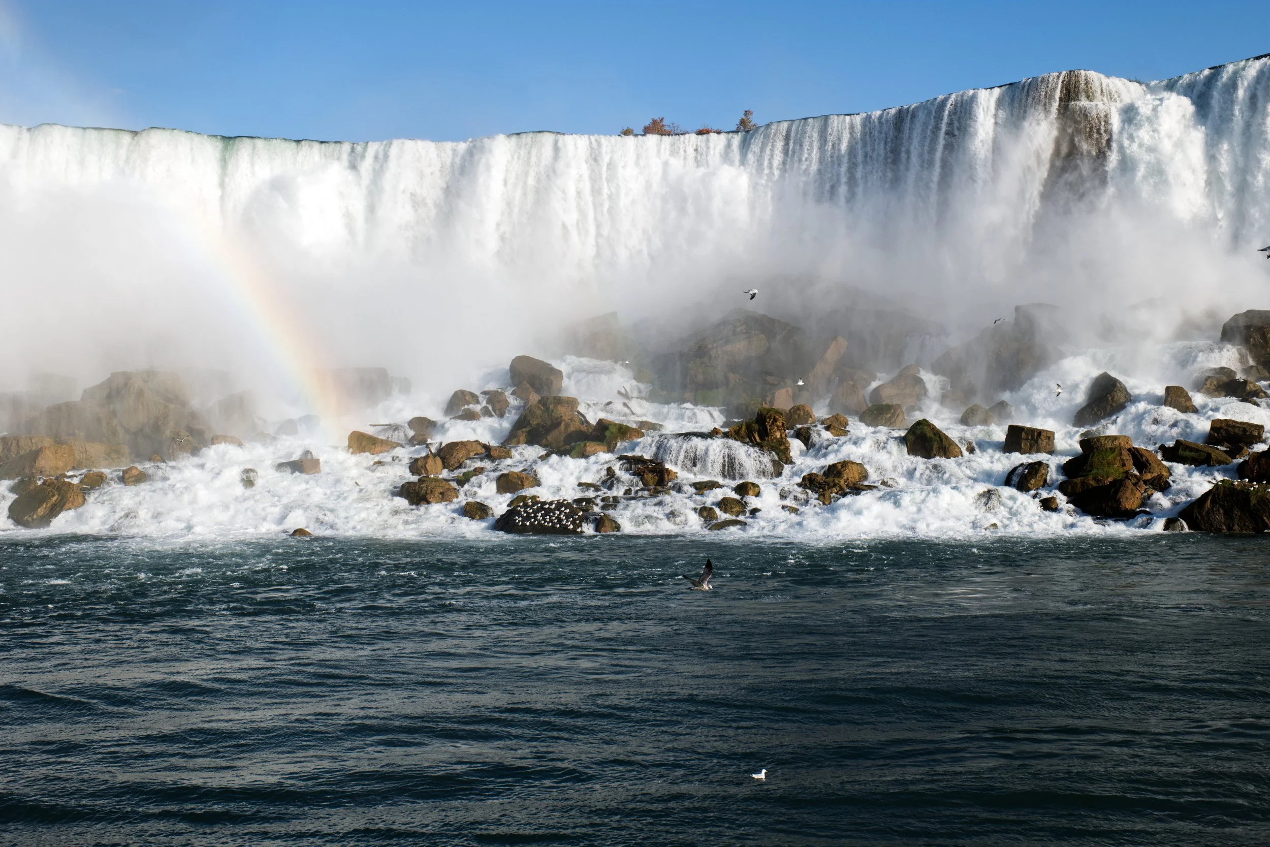 Waterfall with mist and rainbow over rocks and river.