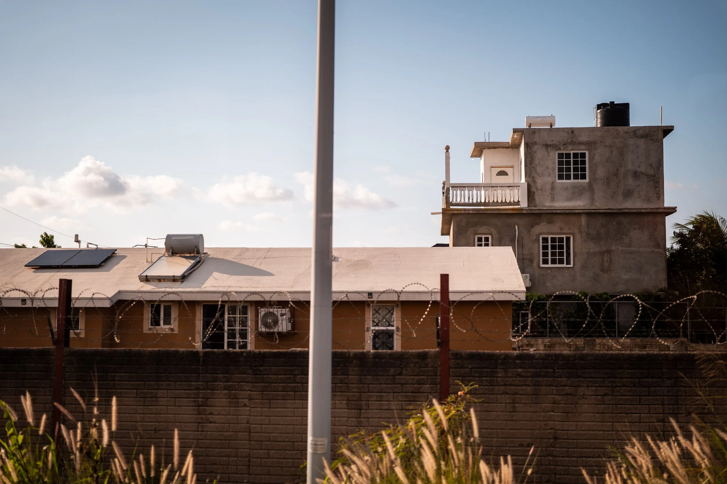 Concrete building with solar panels on the roof, barbed wire fence, and grassy foreground.