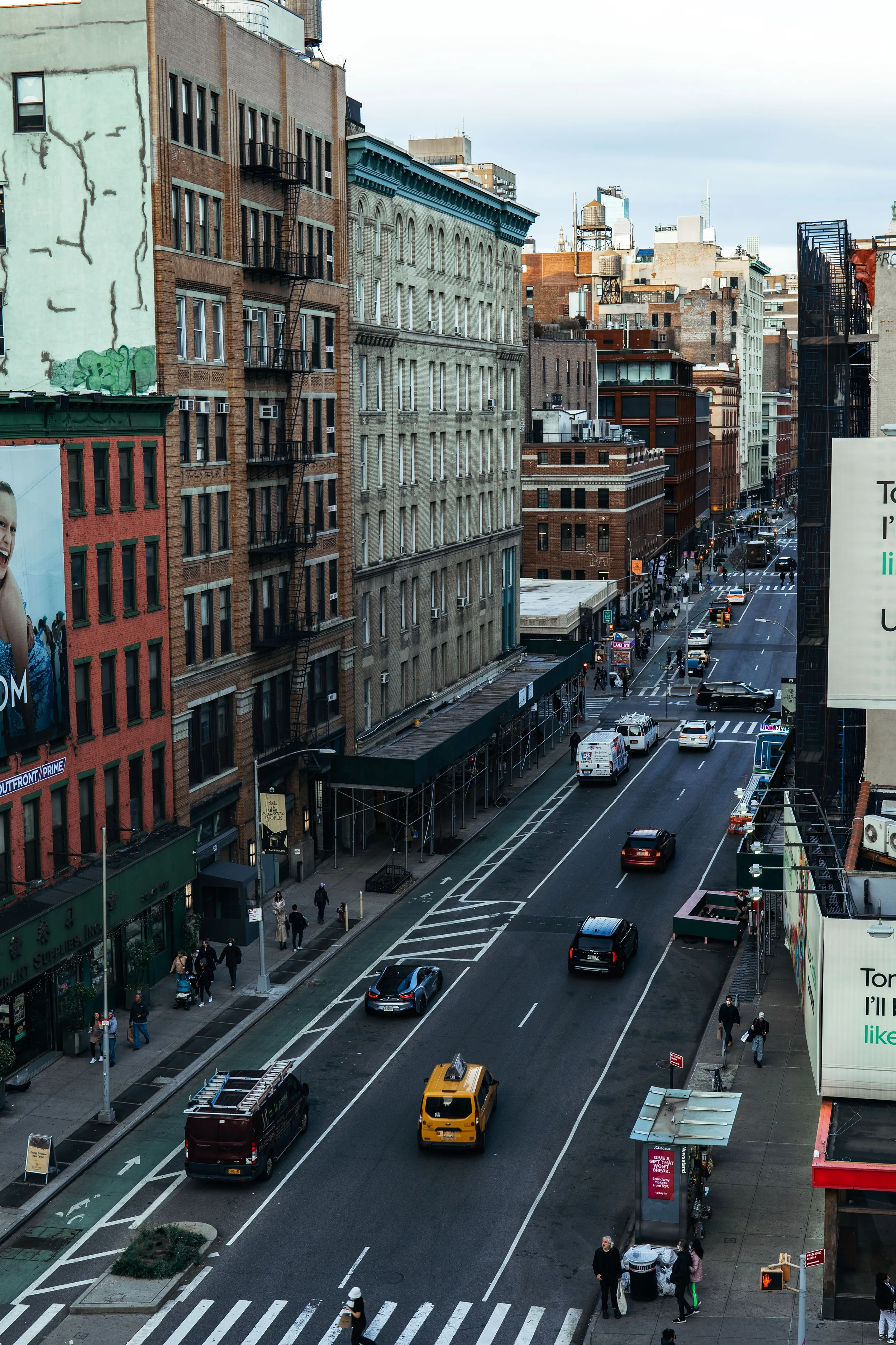 City street with cars and pedestrians, tall buildings, billboards, and a bike lane, viewed from above.