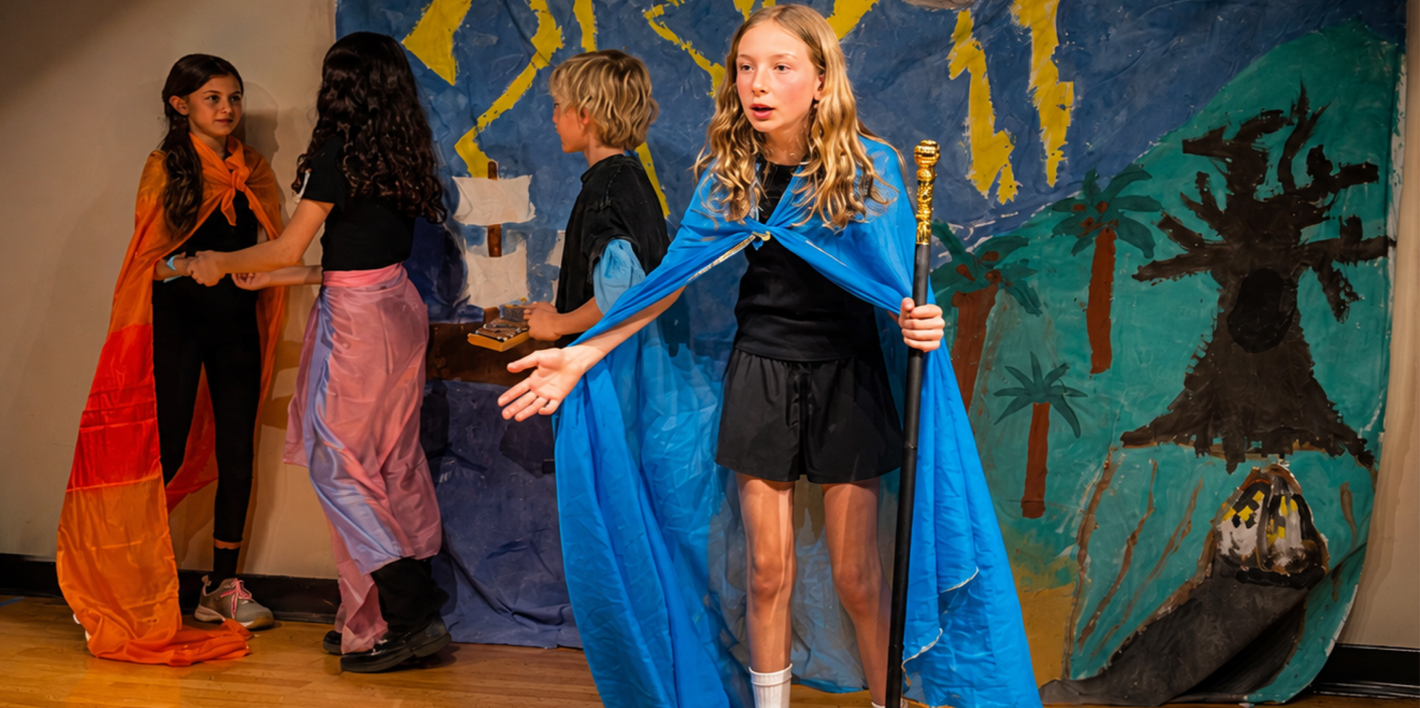 BCSIS students performing a play in front of a hand-painted classroom set.