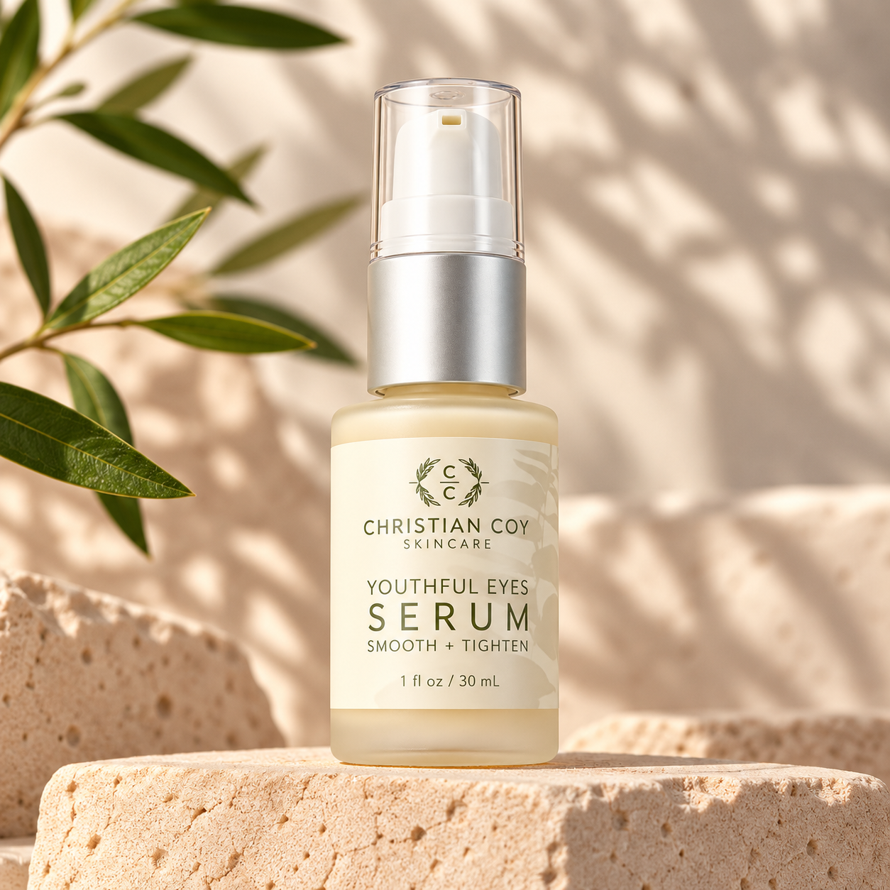 Christian Coy Youthful Eyes Serum displayed on a natural stone pedestal with olive branches and soft botanical shadows against a warm neutral background.