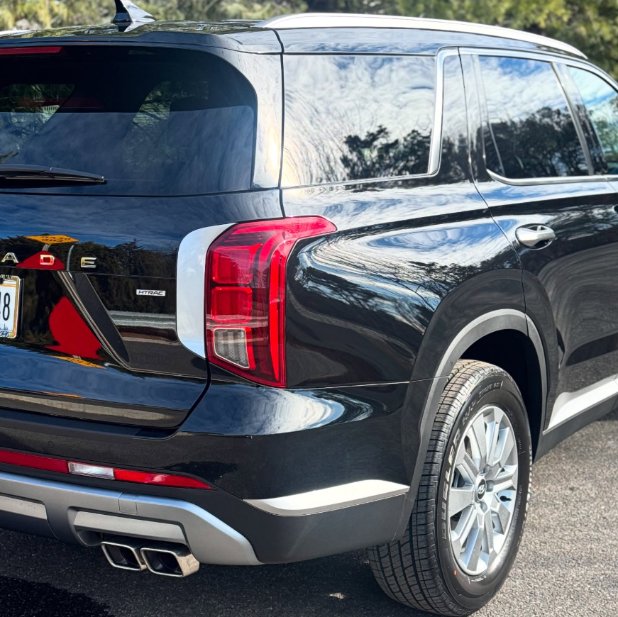 Rear quarter view of a black Hyundai Palisade HTRAC SUV showing LED taillights, dual exhaust tips, and silver alloy wheel