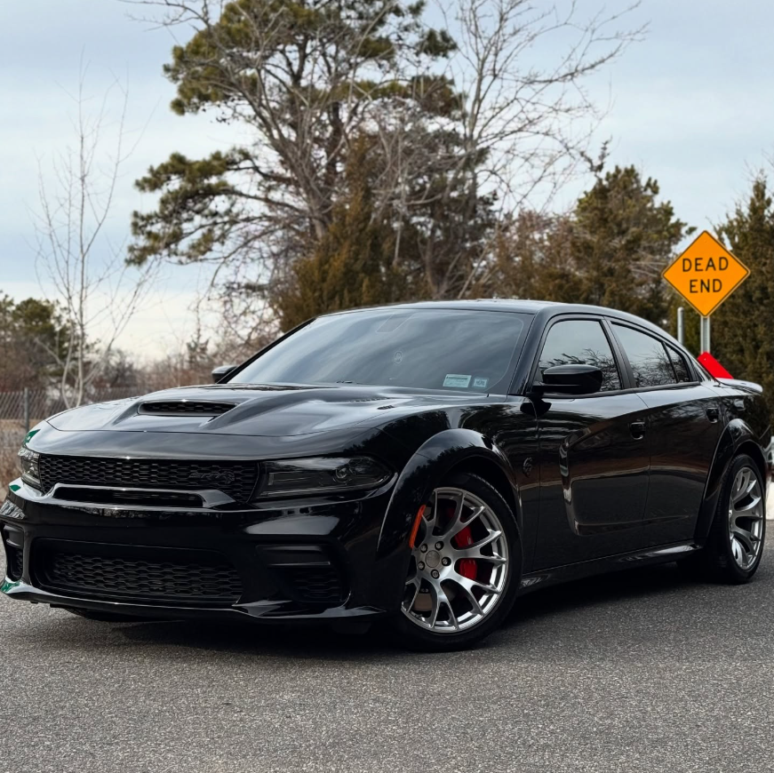 Black Dodge Charger SRT Hellcat with hood scoop, aggressive front fascia, red brake calipers, and gunmetal wheels parked outdoors