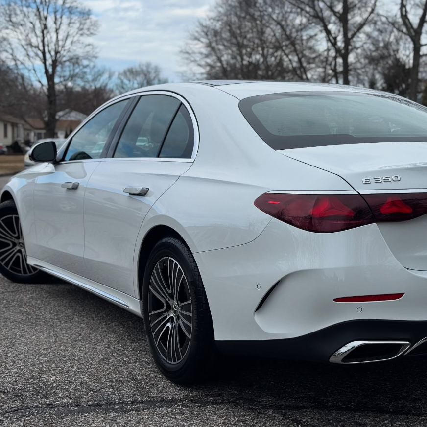 Rear three-quarter view of a white Mercedes-Benz E350 sedan showing LED taillights, chrome exhaust tips, and multi-spoke alloy wheels