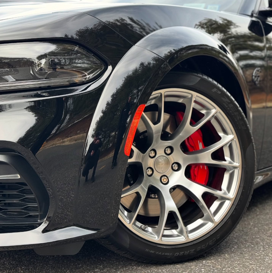 Close-up of a Dodge Charger SRT Hellcat gunmetal split-spoke wheel with oversized red brake caliper and performance tire