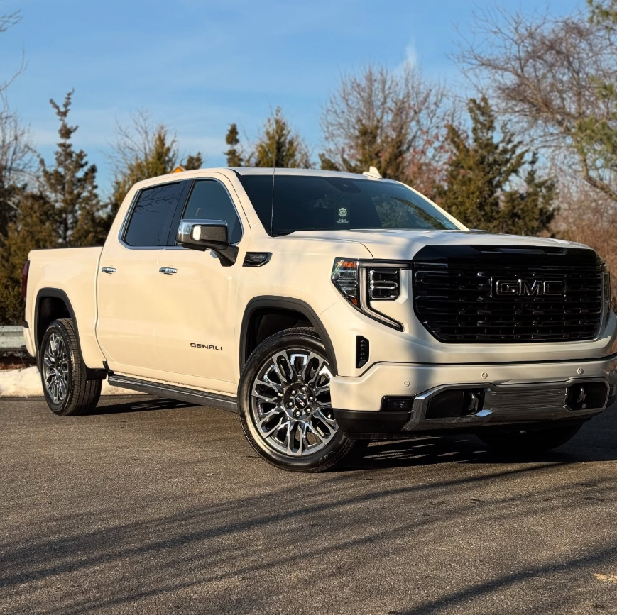 White GMC Sierra 1500 Denali crew cab pickup truck with black grille, chrome accents, and polished multi-spoke wheels parked outdoors on a sunny day