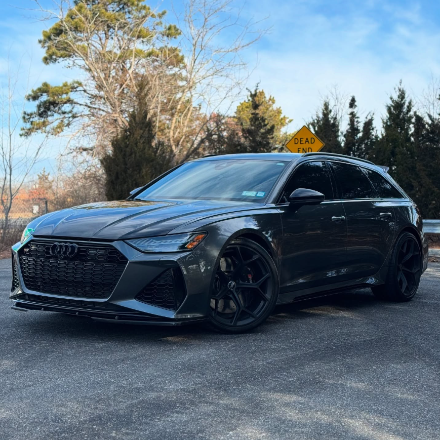 Gray Audi RS6 Avant wagon with aggressive front splitter, black honeycomb grille, red brake calipers, and gloss black wheels parked outdoors