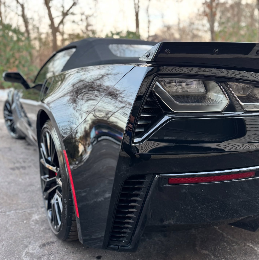 Rear quarter detail of a black Chevrolet Corvette C7 convertible showing angular taillights, rear spoiler, side vents, and soft top