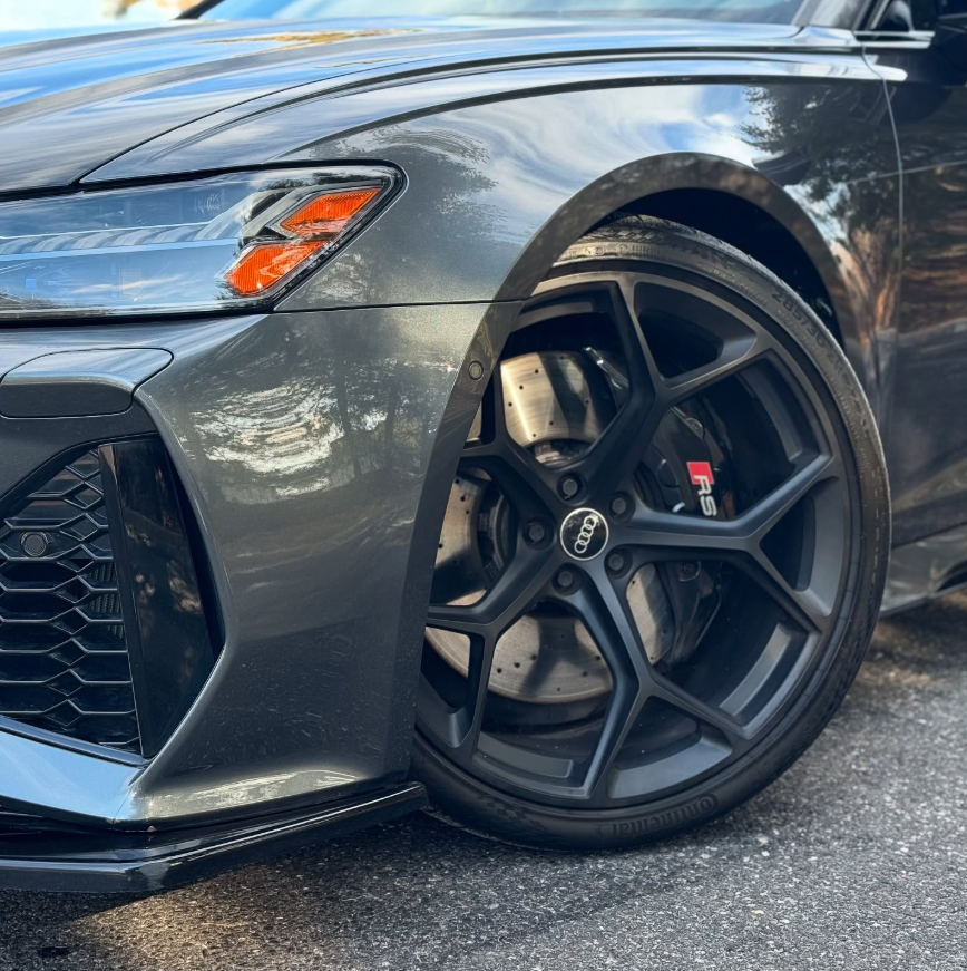 Close-up of a gloss black Audi RS6 Avant wheel with RS-badged brake caliper, drilled rotor, and low-profile performance tire