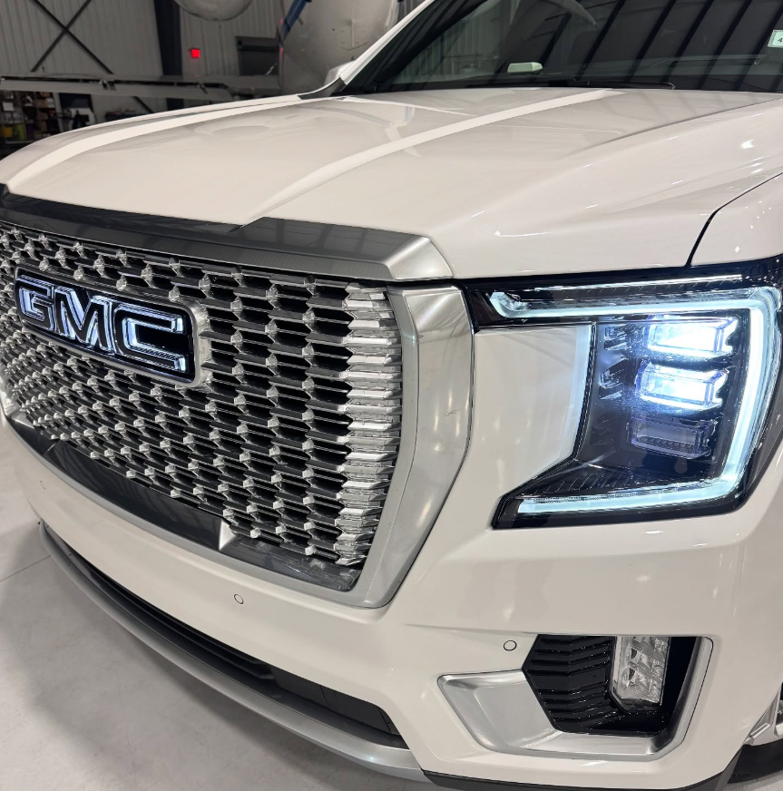 Close-up of a white GMC Yukon Denali featuring a chrome billet grille, illuminated GMC badge, and LED signature headlights