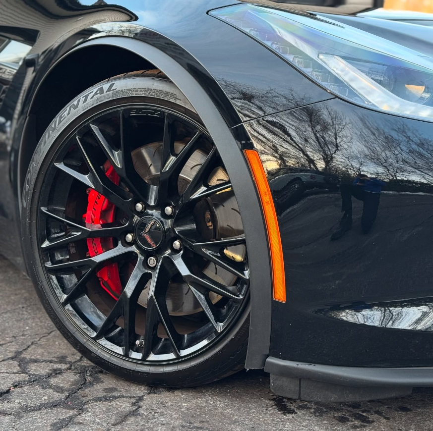 Close-up of a black Chevrolet Corvette C7 gloss black multi-spoke wheel with red brake caliper, slotted rotor, and Continental performance tire