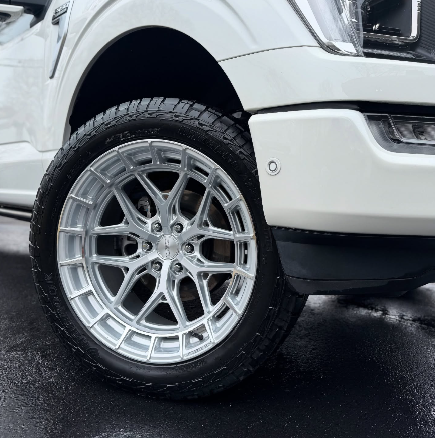 Close-up of a polished aftermarket multi-spoke alloy wheel with all-terrain tire on a white Ford F-150 Limited