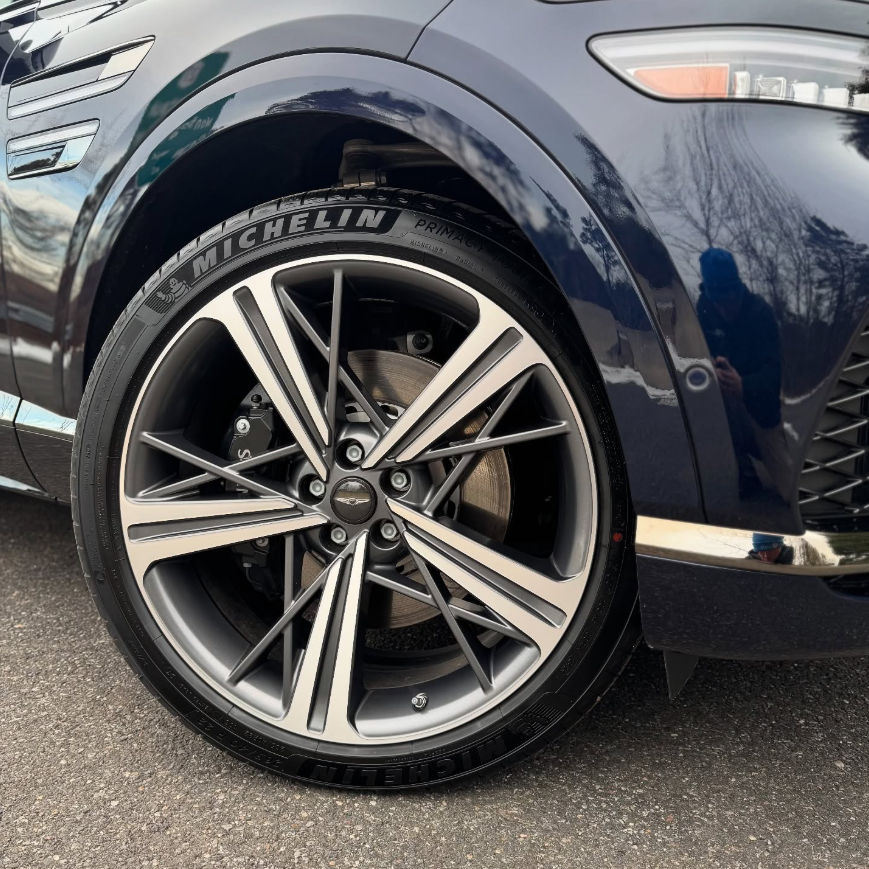Close-up of a Genesis GV80 two-tone dark gray multi-spoke alloy wheel with Michelin Primacy tire and large vented brake rotor