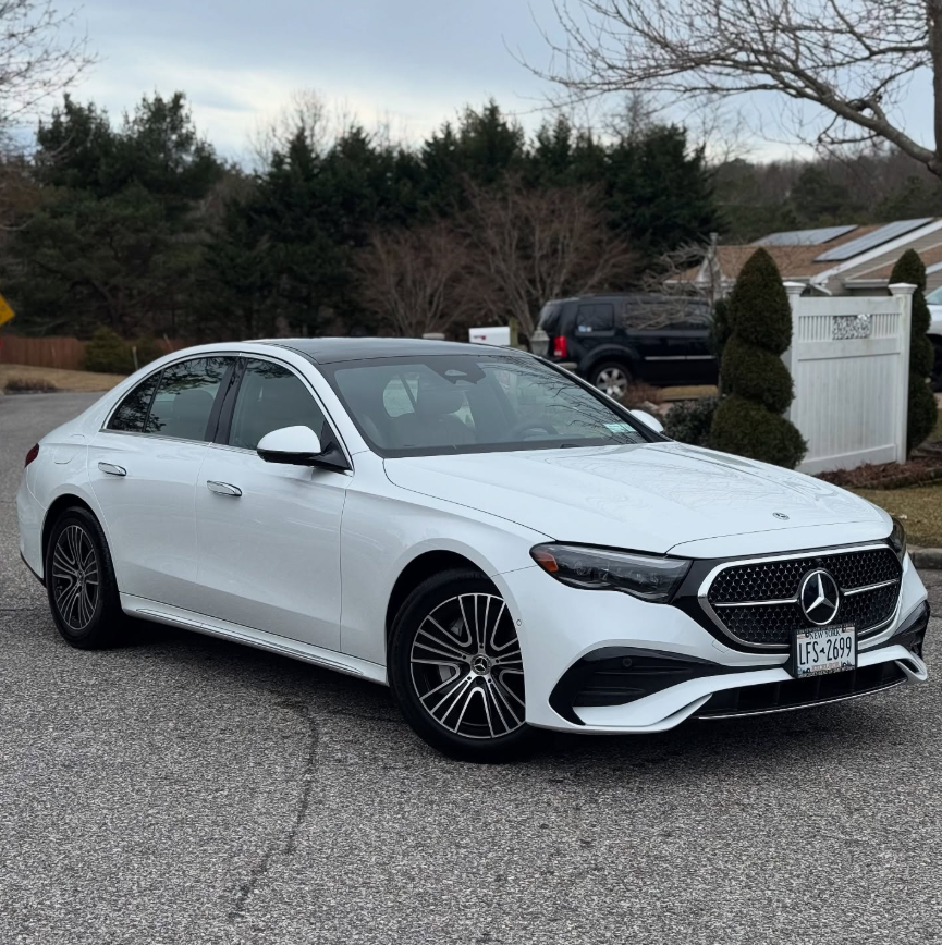 White Mercedes-Benz E-Class sedan with AMG styling package, mesh grille, and multi-spoke alloy wheels parked in a residential driveway