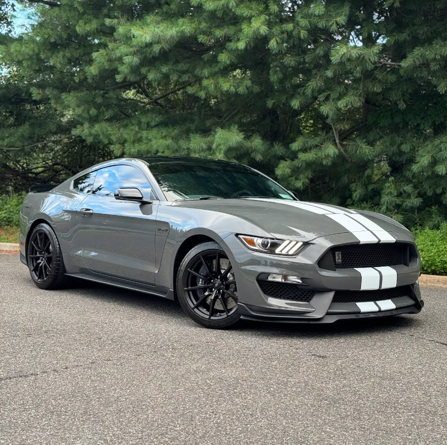 Gray Ford Shelby GT350 Mustang coupe with white racing stripes and black wheels parked outdoors