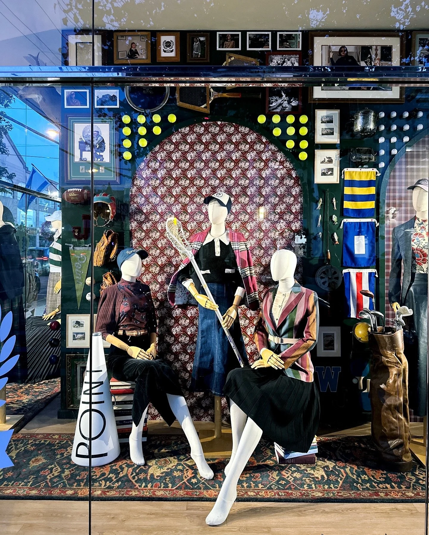A study in collegiate tradition and country club heritage. This window brings together vintage sport and leisure artifacts&mdash;lacrosse sticks, tennis rackets, golf bags, and cheer megaphones&mdash;curated to evoke the spirit of campus life and tim