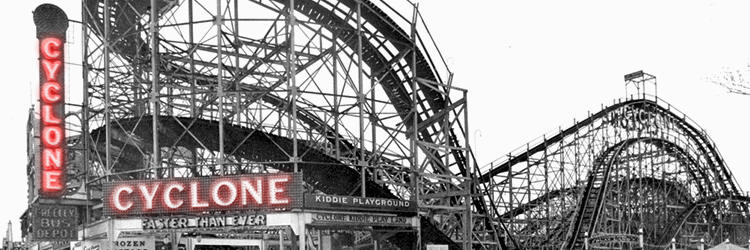 A black and white photo of a wooden roller coaster at an amusement park, with a neon sign reading 'Cyclone' and a Kiddie Playground sign nearby.