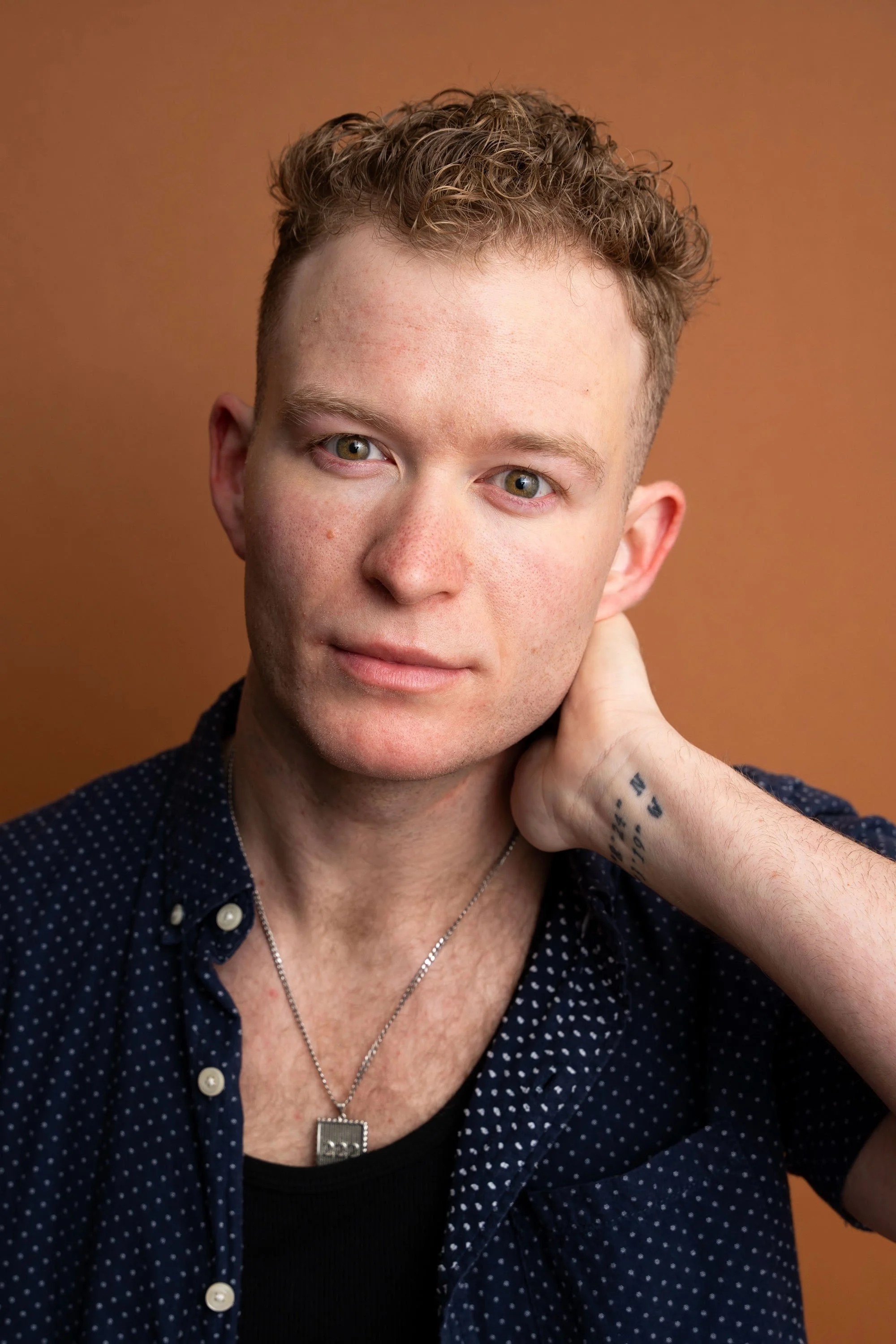 Smiling man with a blue button-up shirt against a dark background.