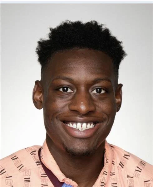 Smiling person with short hair wearing a patterned shirt.