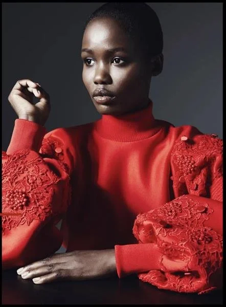 Person wearing a red sweater with ornate embroidered sleeves, looking to the side with a thoughtful expression.