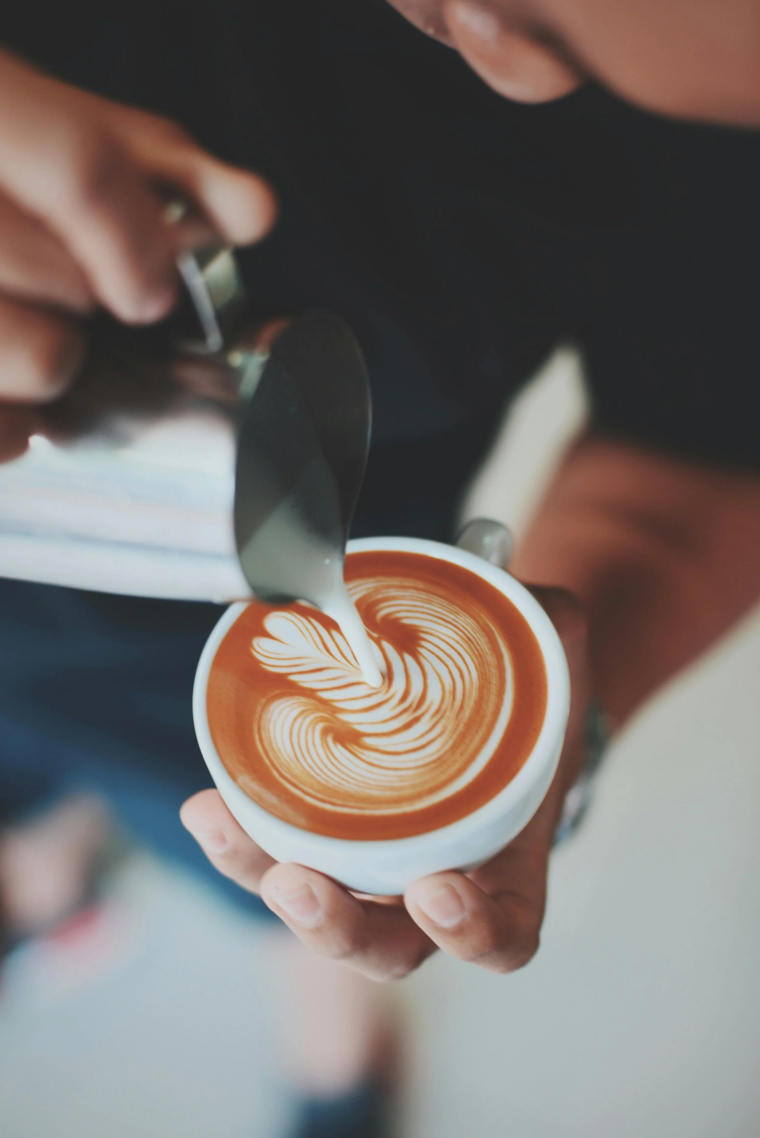Person pouring latte art into a cup of coffee.