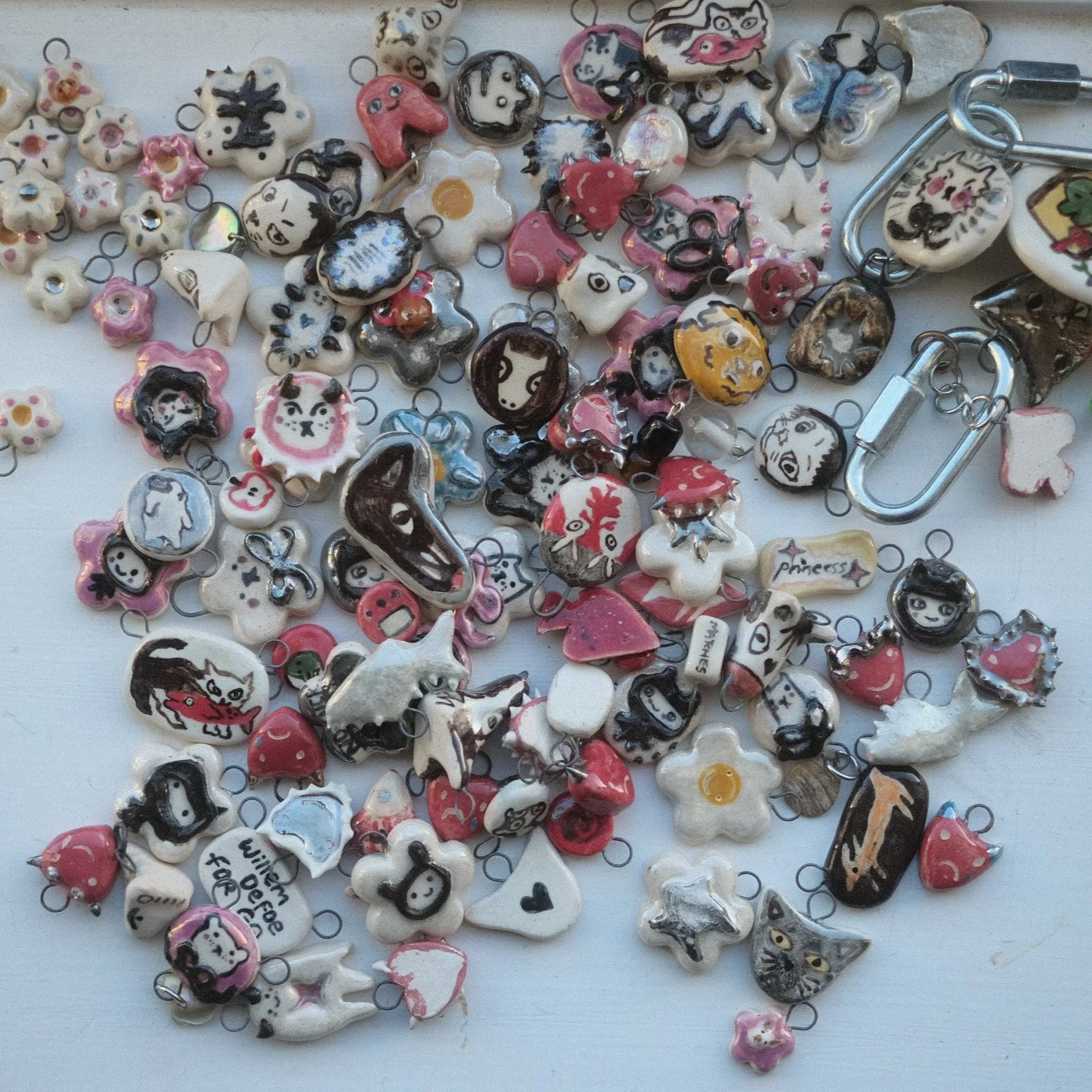 A collection of various small, colorful charms and keychains with different designs, including animals, faces, hearts, and words, scattered across a white surface.