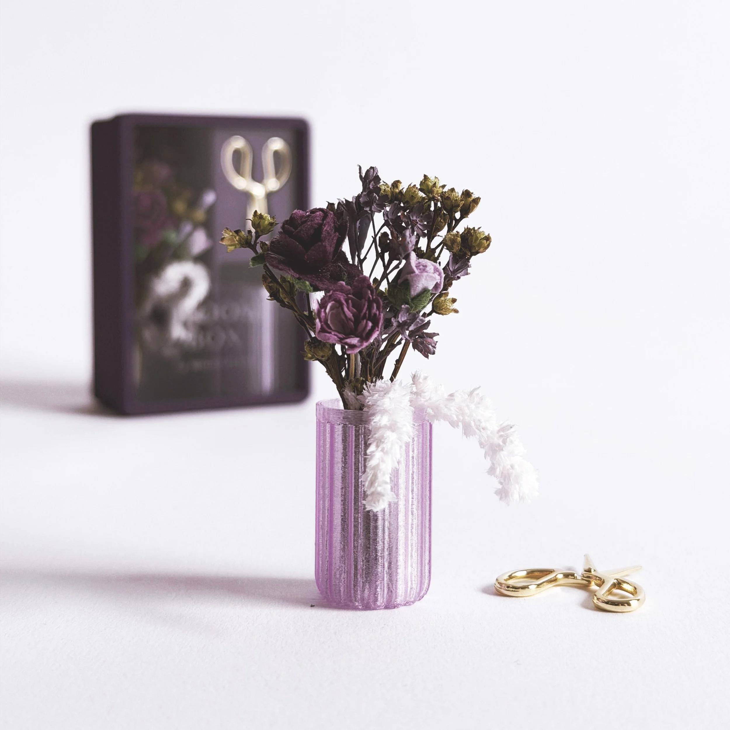 Close-up of purple miniature floral arrangement with gypsophila, roses, and trailing amaranthus in small vase