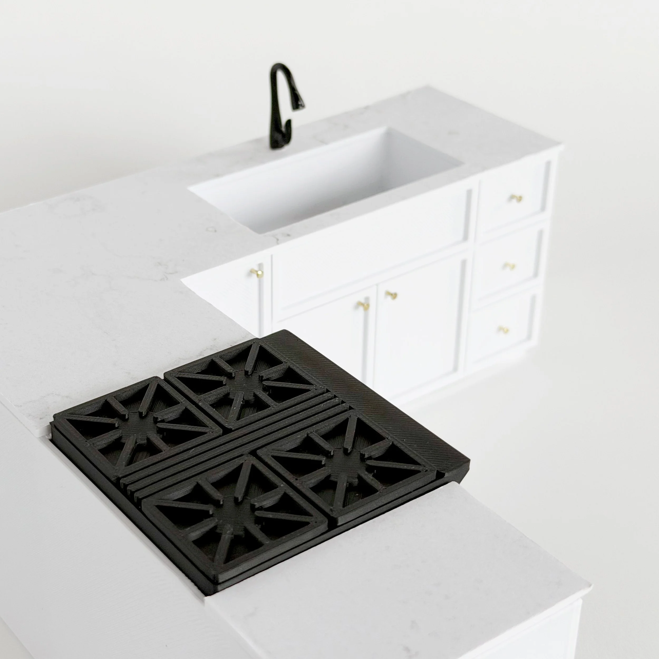 Miniature black gas-style oven with opening door and movable racks, shown beside white dollhouse kitchen cabinets.