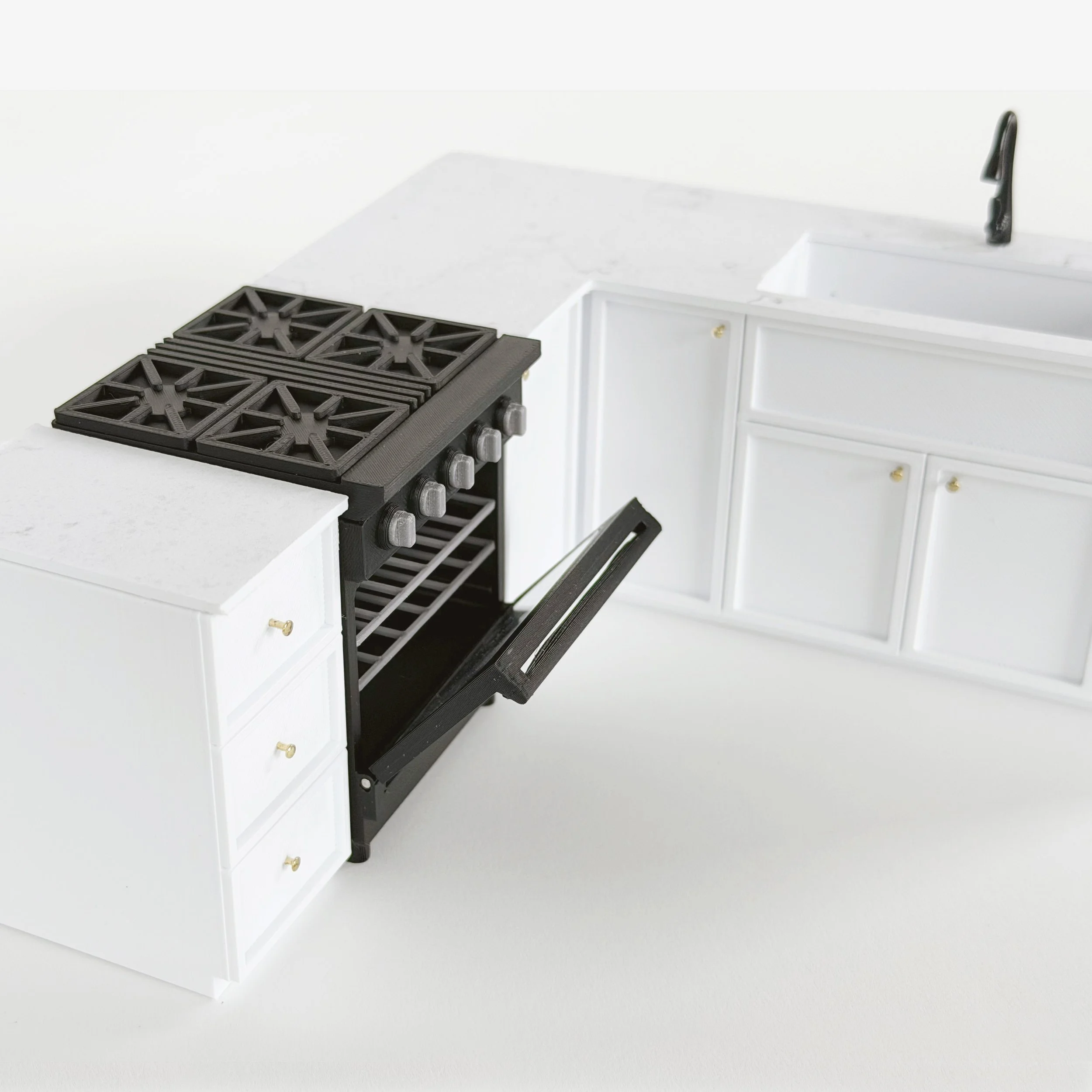 Miniature black gas-style oven with opening door and movable racks, shown beside white dollhouse kitchen cabinets. (Copy)